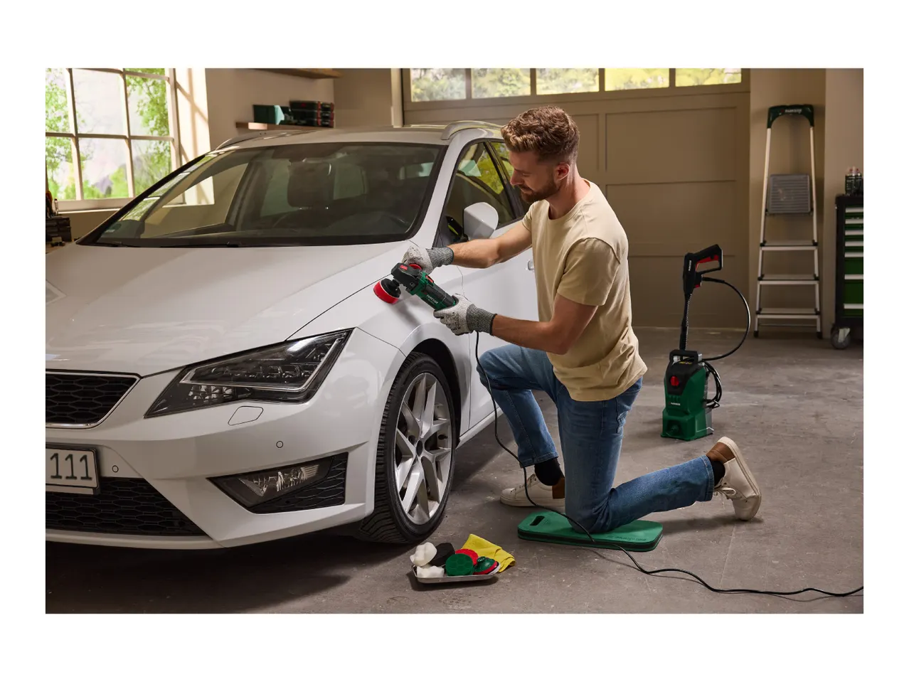 Man polishing a white car with an electric polisher in a garage.