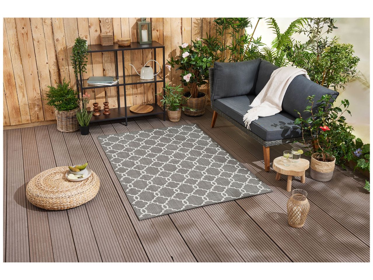 Tapis gris clair à motif géométrique placé dans un salon avec canapé et plantes.