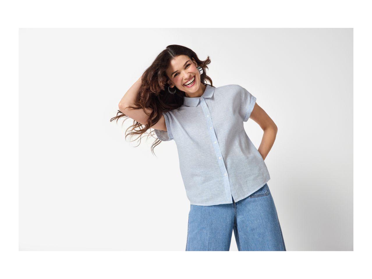 Woman in a light blue striped short-sleeve shirt and denim culottes, smiling brightly.