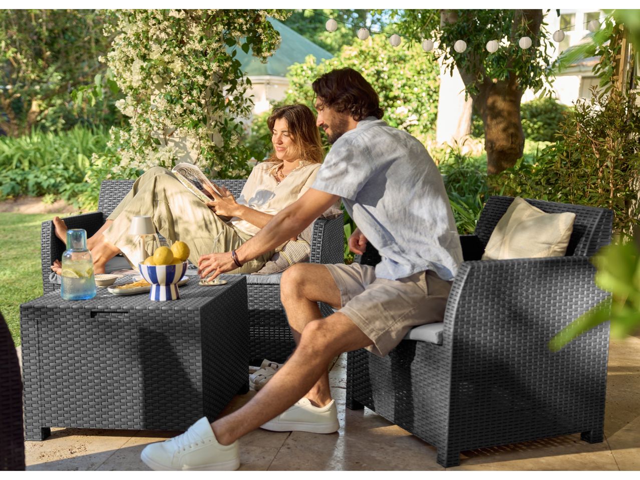 Couple relaxing on a dark grey rattan garden furniture set with drinks and lemons.