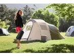 Woman holding a CRIVIT sleeping bag next to a tent at a campsite.