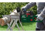 Person cutting a log with a chainsaw on a sawhorse in a garden.