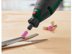 Rotary tool with a pink grinding stone sharpening scissors on a wooden surface.