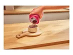 Hand pouring red beans from a pink container into a patterned bowl on a wooden board.