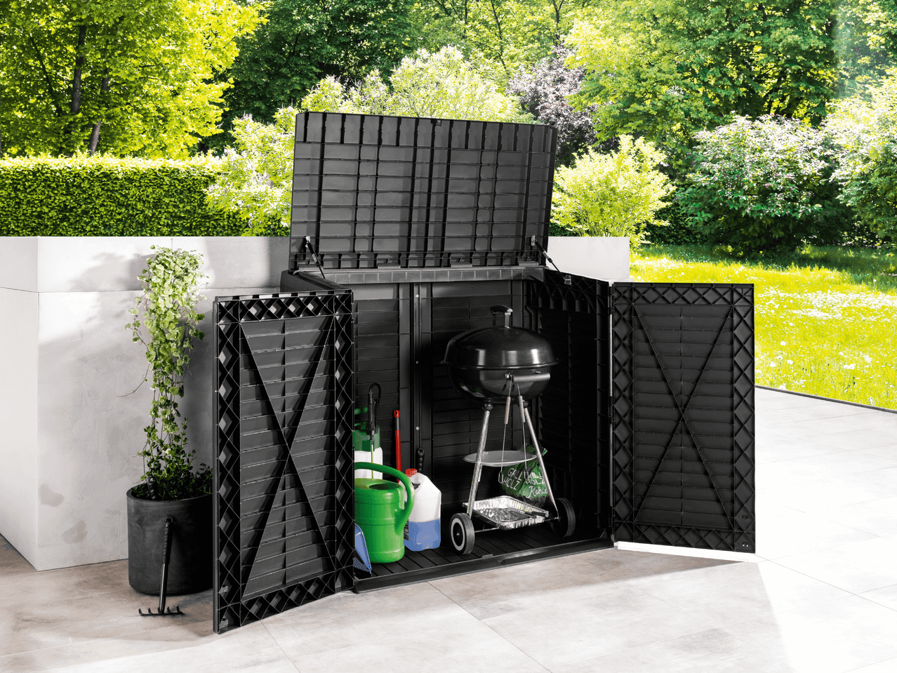 Schwarze Gartenbox mit Grill, Gießkanne und Gartengeräten auf einer Terrasse mit viel Grün.