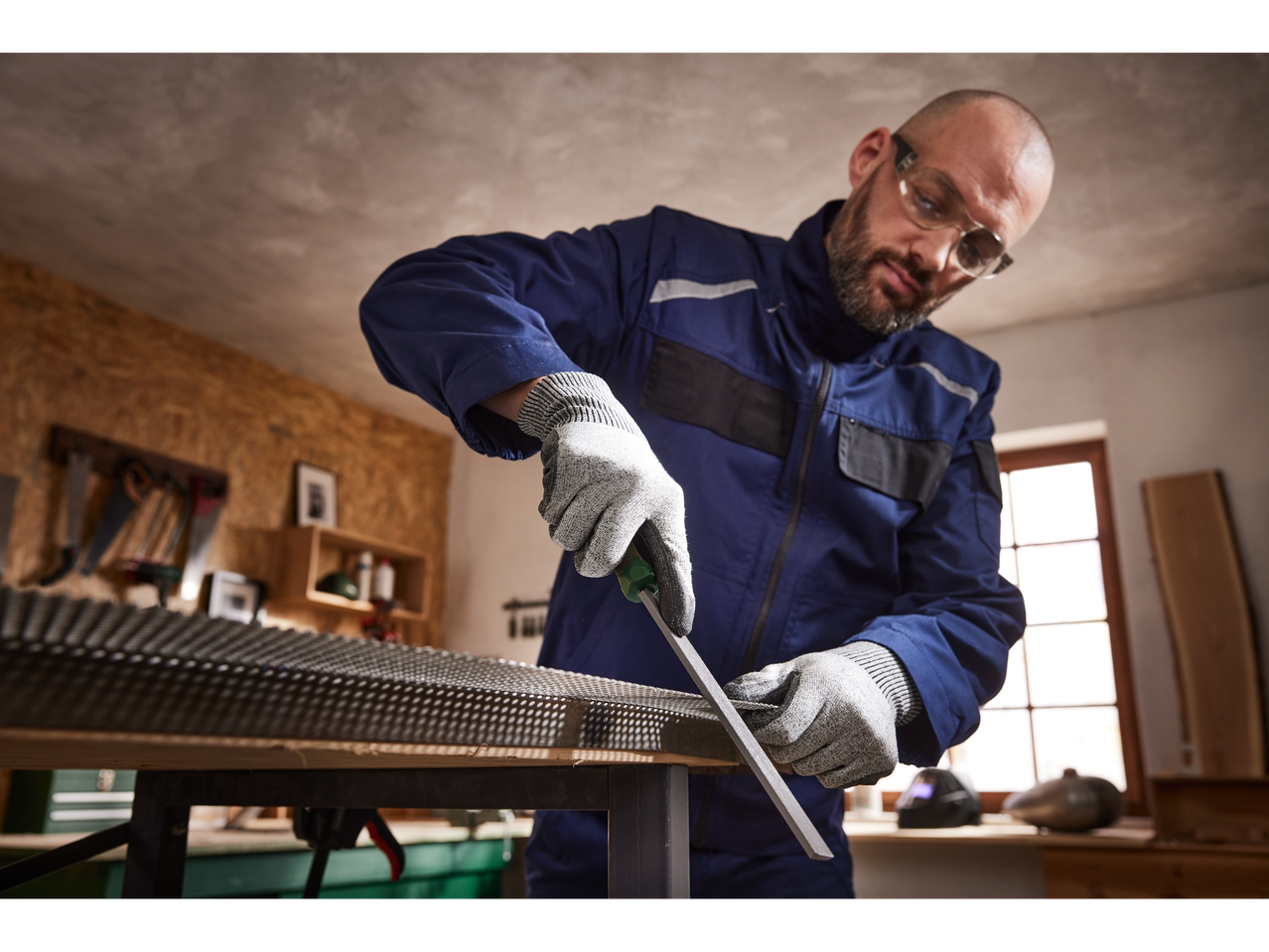 A man in work clothes and safety glasses using a PARKSIDE® File Set on a metal sheet.