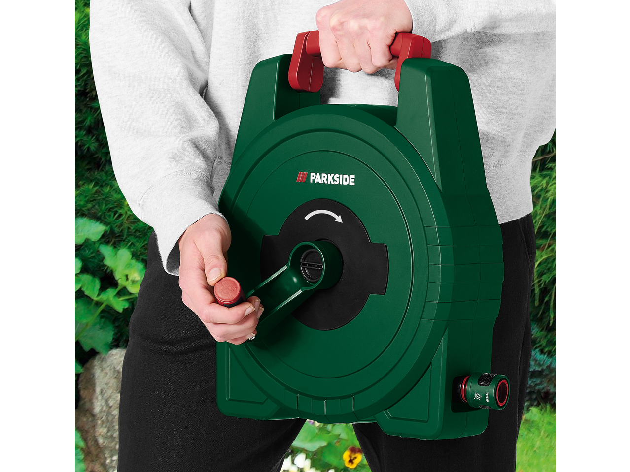 Pessoa segurando um enrolador de mangueira de jardim manual verde com manivela.