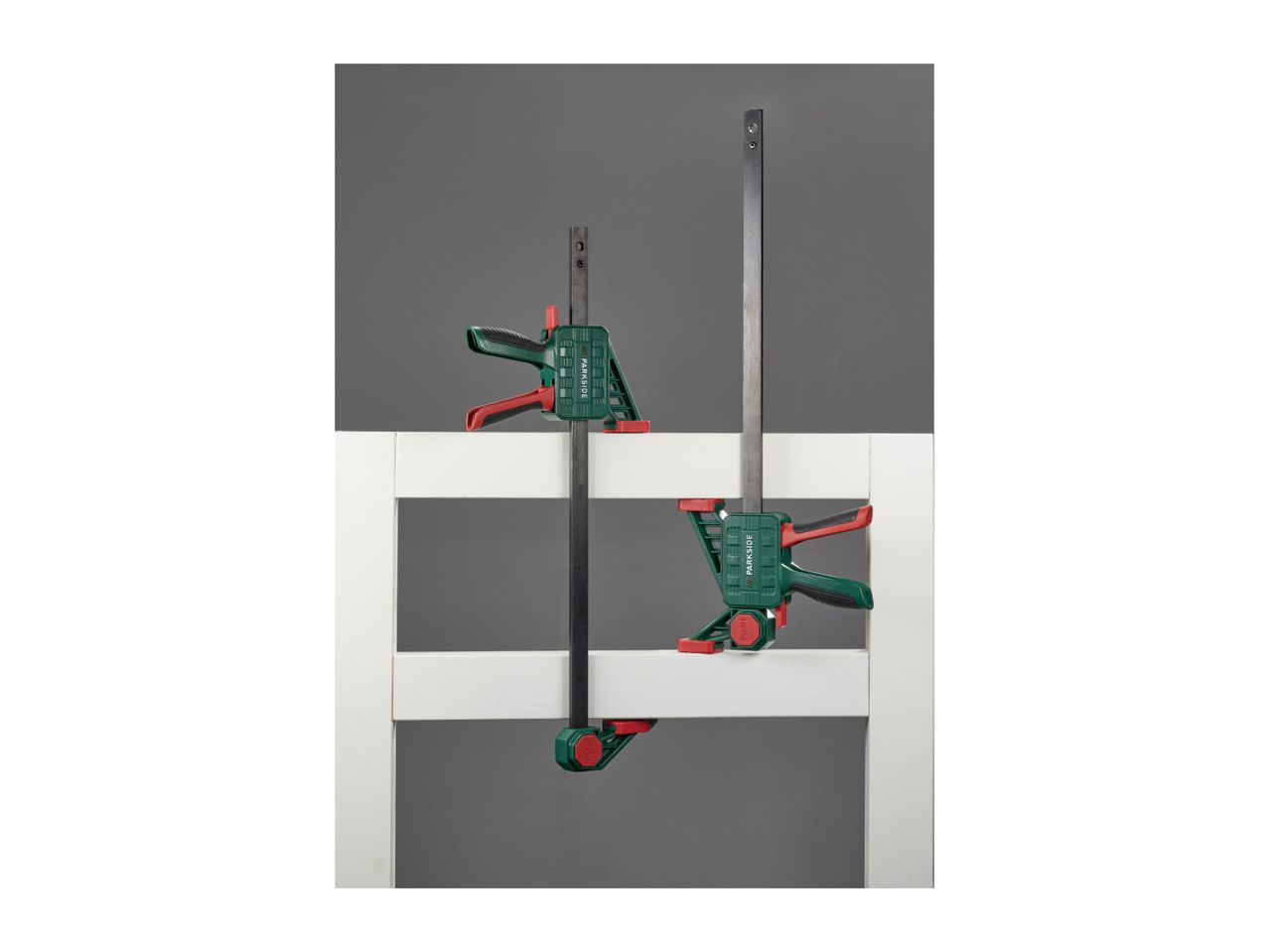 Two bar clamps, one larger and one smaller, securing white wooden planks.