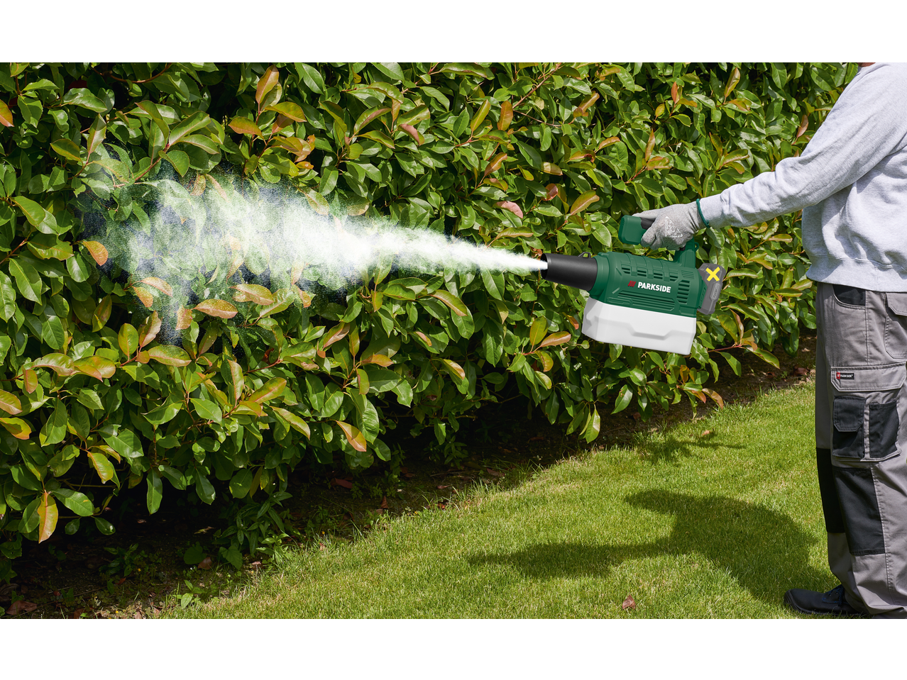 Bărbat folosește un pulverizator cu baterii pentru a stropi un tufiș verde.
