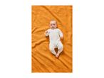 Baby in a white sleepsuit with stars, lying on an orange waffle blanket.