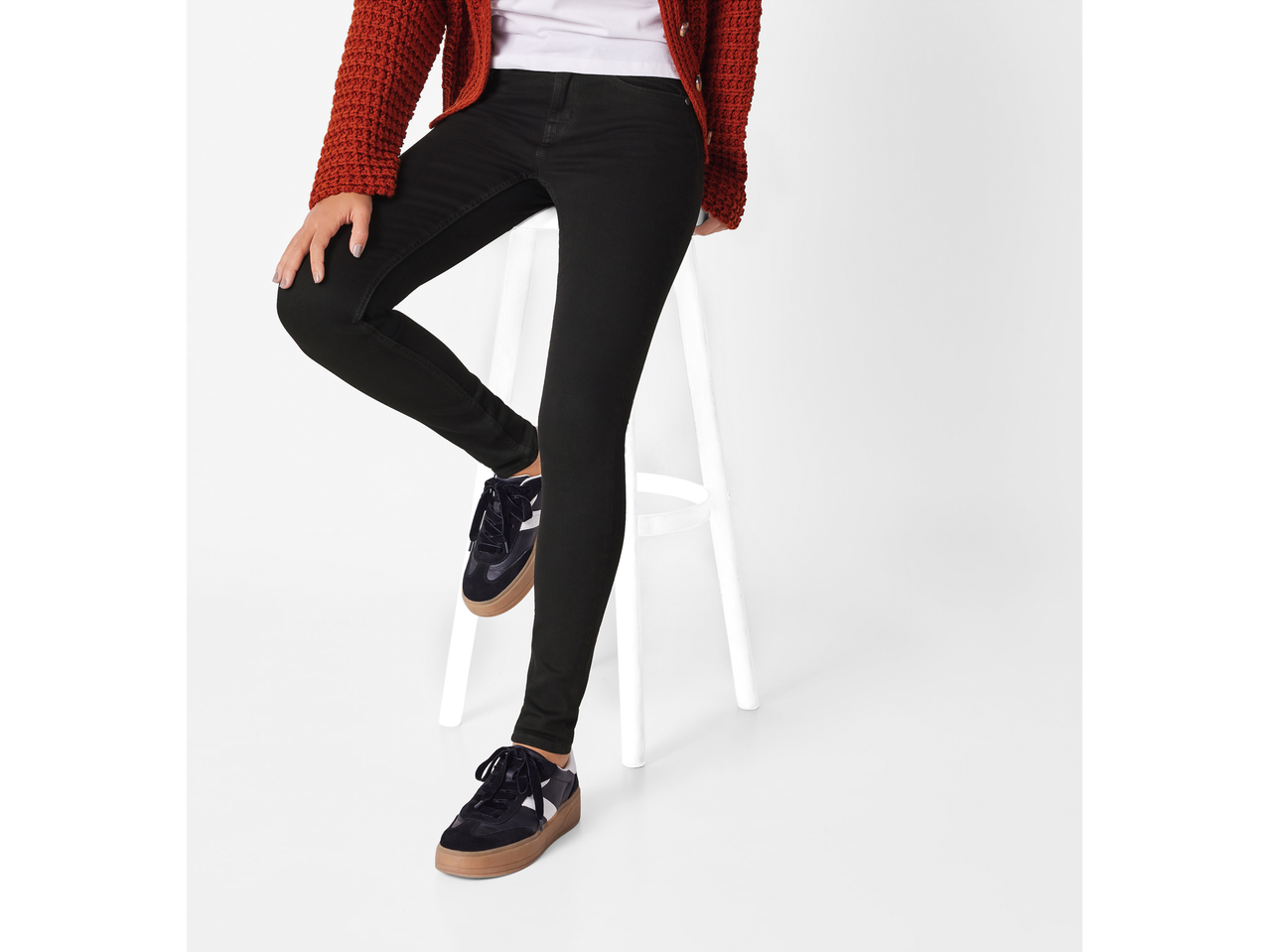 Woman wearing black super skinny fit jeans, a white top, and a rust-colored cardigan.