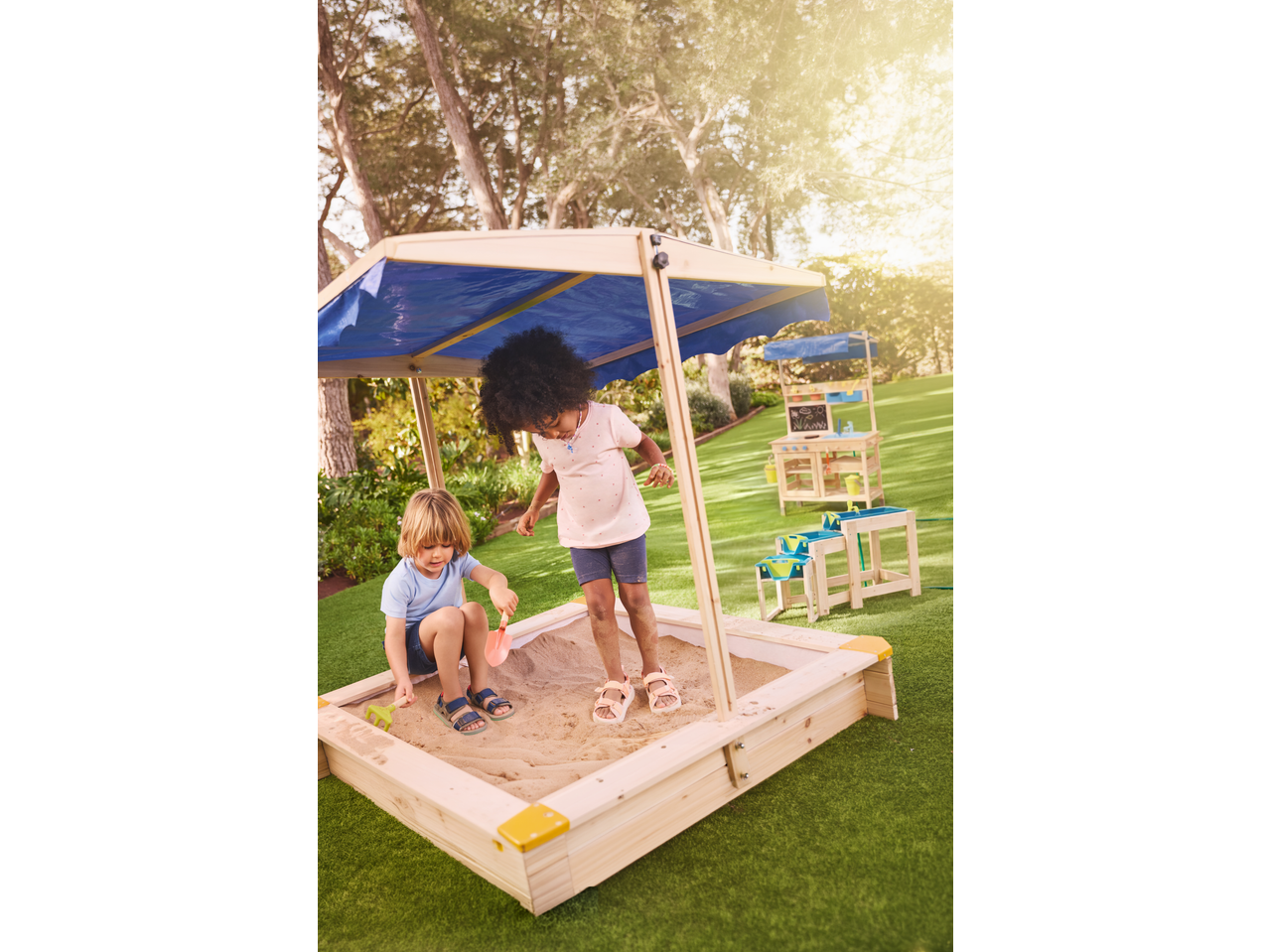 Children playing in a LUPILU sandbox with blue sunshade and sand toys.