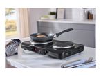 Portable electric hob with a frying pan cooking food, on a kitchen counter.