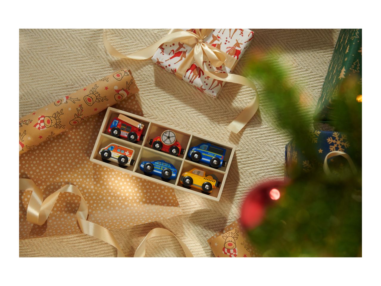 Christmas gifts: a wooden toy car set, reindeer wrapping paper, and a decorated tree.