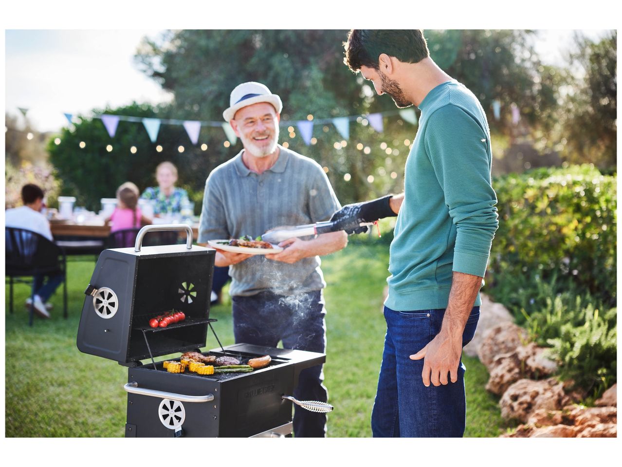 Deux hommes cuisinent sur un barbecue Weber dans un jardin.