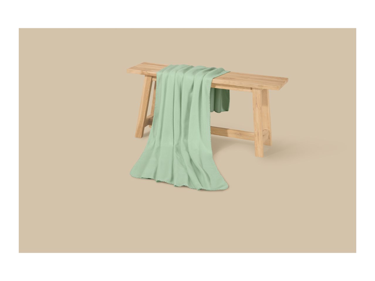 Light green blanket draped over a wooden bench on a beige background.
