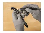 Hands in gloves polishing a watch with a rotary tool.