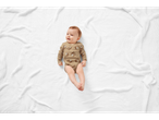 Baby in a brown bear-print onesie lying on a white knitted blanket.