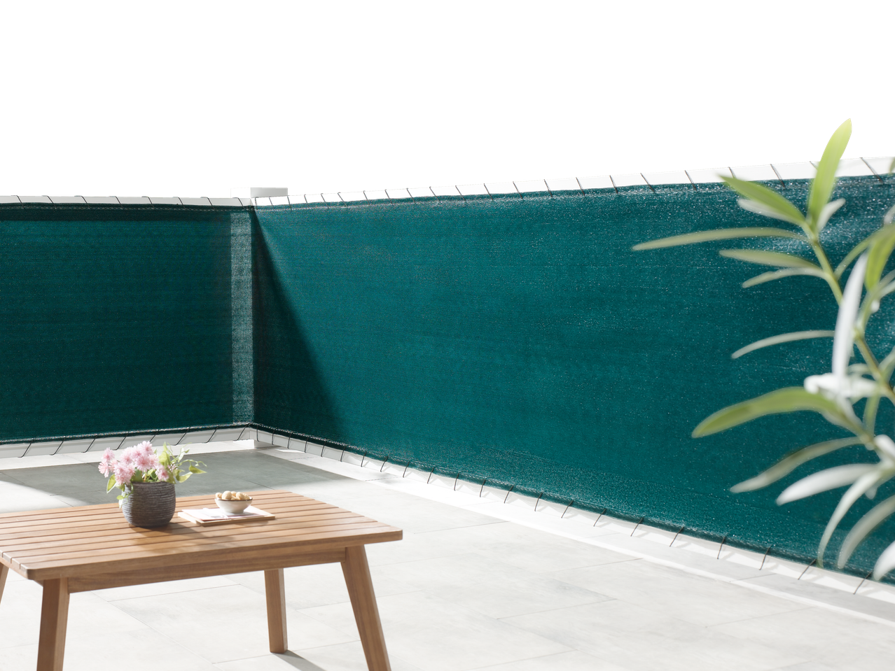 Livarno Balcony/Fence Privacy Screen in dark green, with a wooden table and plant on a patio.