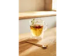A glass of tea with red berries and mint on a wooden table.