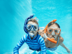 Zwei Kinder mit Schnorchelmasken und Schnorcheln schwimmen unter Wasser.