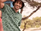 Mann in grünem Poloshirt mit Muster und Fischerhut.