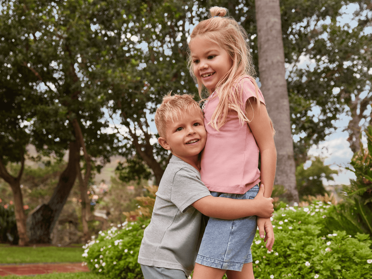 Zwei Kinder in T-Shirts und Shorts umarmen sich im Garten.