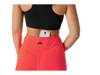 Femeie purtând un sutien sport negru și leggings coral cu talie înaltă, cu un telefon în buzunar.