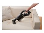 Handheld cordless vacuum cleaner being used to clean crumbs off a beige sofa