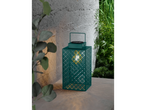 Green outdoor lantern with patterned design and light casting shadows on a concrete surface.