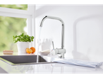 A modern chrome kitchen faucet with a high-arc spout, dispensing water into a stainless steel sink.