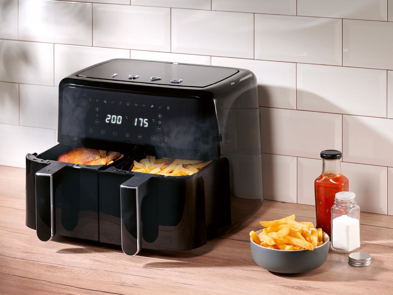 Черен фритюрник с две кошници, пълен с пържени картофи и пиле, на дървен плот.