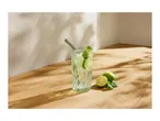 Refreshing drink with lime, mint, and ice in a patterned glass with a straw on a wooden surface.