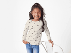 Ein lächelndes Mädchen in einem cremefarbenen Langarmshirt mit Blumenmuster und Jeans.