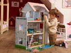 Toddler playing with a large wooden dollhouse in a child's room.