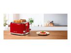 Red retro toaster with four slots on a wooden table next to a prepared toast