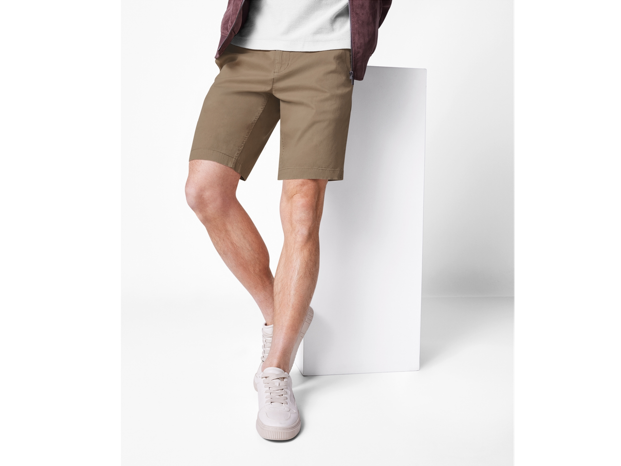 Un bărbat poartă pantaloni scurți kaki și adidași albi.