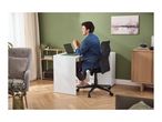 Man working on a laptop at a white desk in a modern living room with green walls.