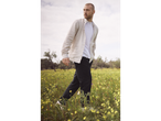 Man walking through a field of flowers wearing a linen shirt and black pants.
