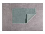 A light green bath mat with a textured surface, partially folded, on a gray tiled floor.
