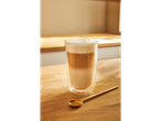 Um copo de latte macchiato com uma colher dourada numa mesa de madeira.