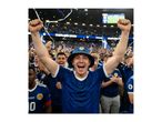 Excited man in a blue bucket hat and jersey celebrating at a stadium with confetti falling.