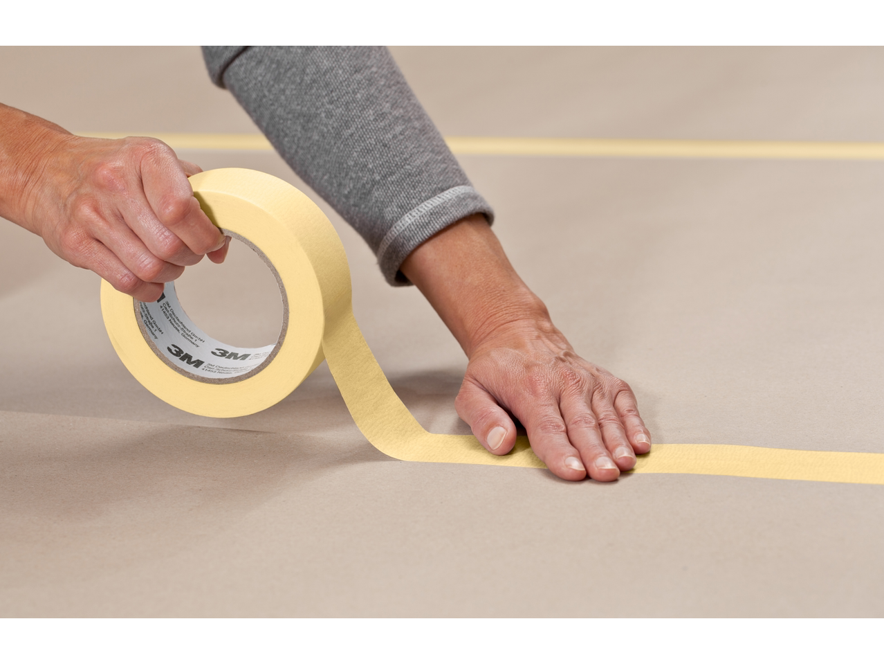 Handen brengen 3M afplaktape aan op een oppervlak, met zichtbare '3M' tekst.