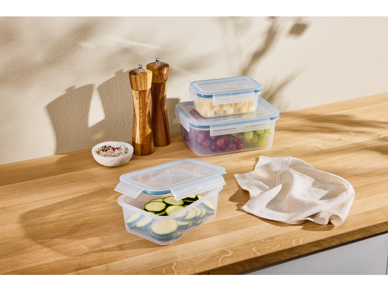 Food storage containers with grapes, cheese, and zucchini, alongside salt and pepper mills.