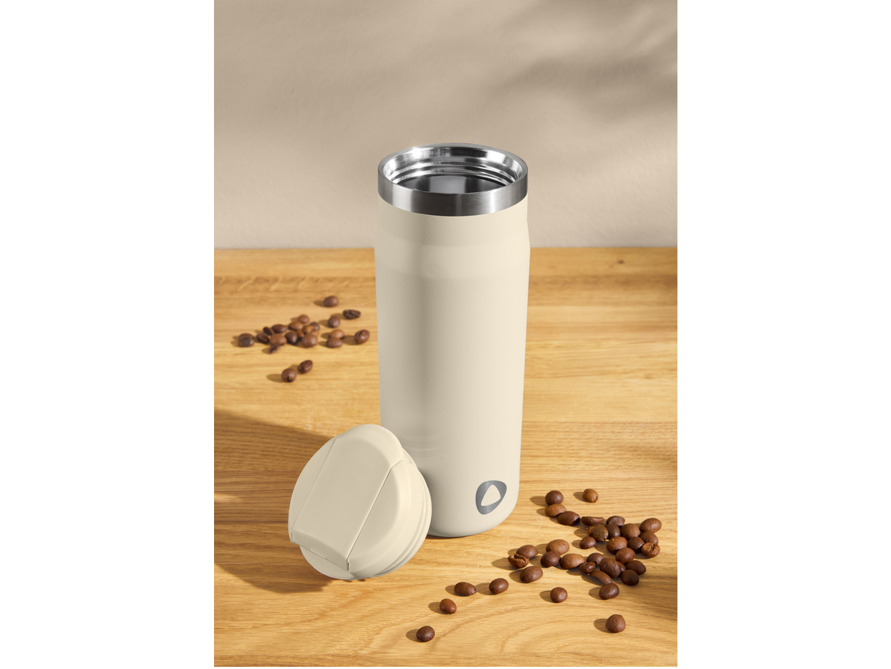 Termos de cafea bej cu boabe de cafea pe o masă de lemn.