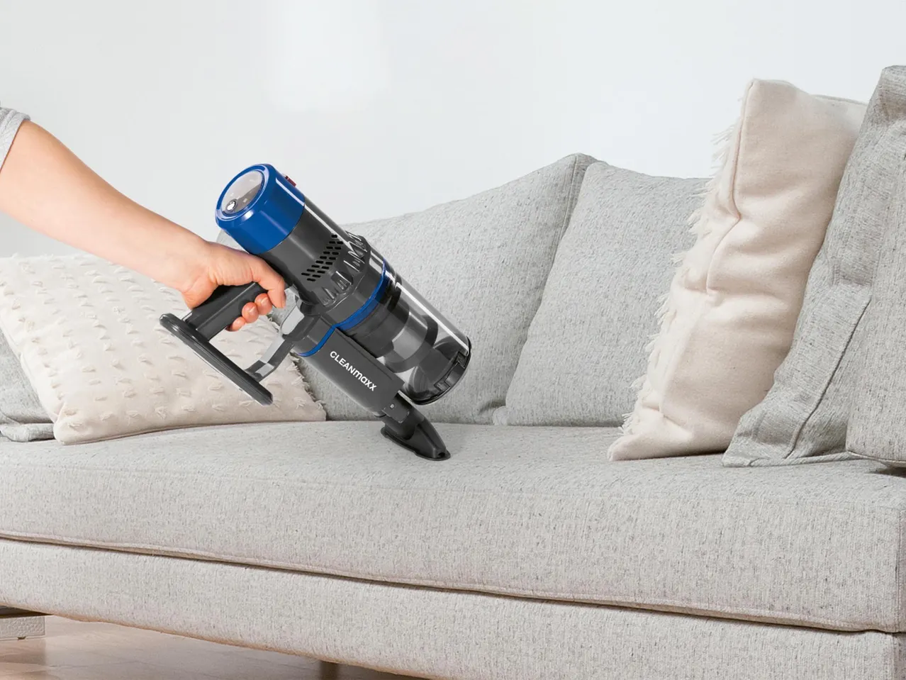 CLEANMAXX kézi porszívóval tisztítanak egy világos kanapét.