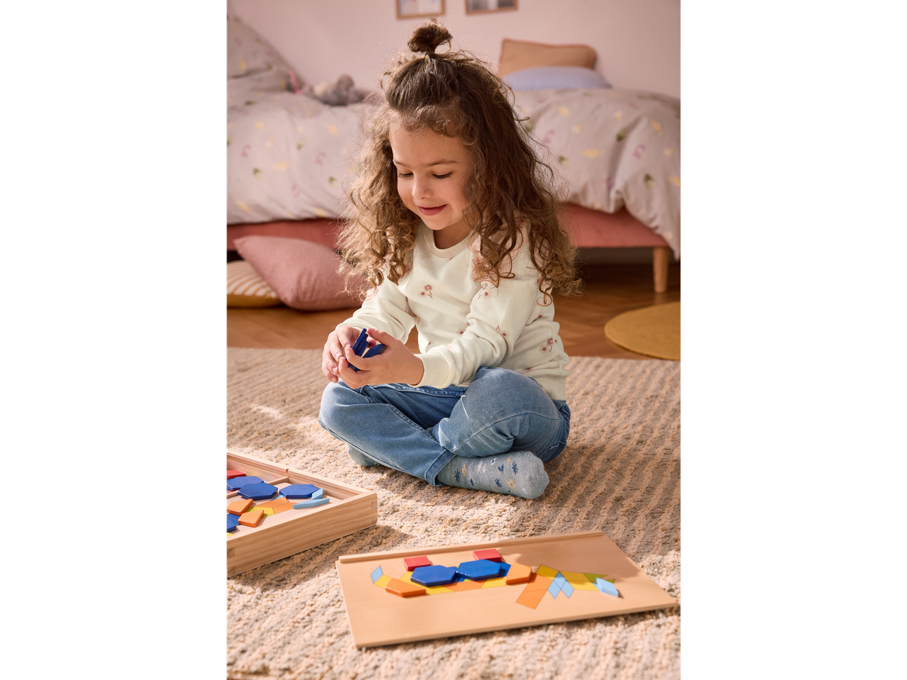 A young girl plays with a colorful wooden pattern block set on a rug.