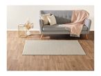 A light grey sofa with decorative pillows and a pink throw blanket on a wooden floor with a rug.