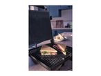 Two grilled sandwiches with prosciutto and arugula on a sandwich maker in a kitchen.