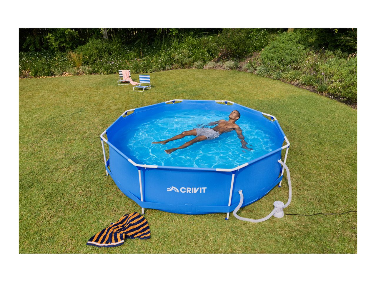 Man relaxing in a blue above-ground pool in a garden with two striped beach chairs.